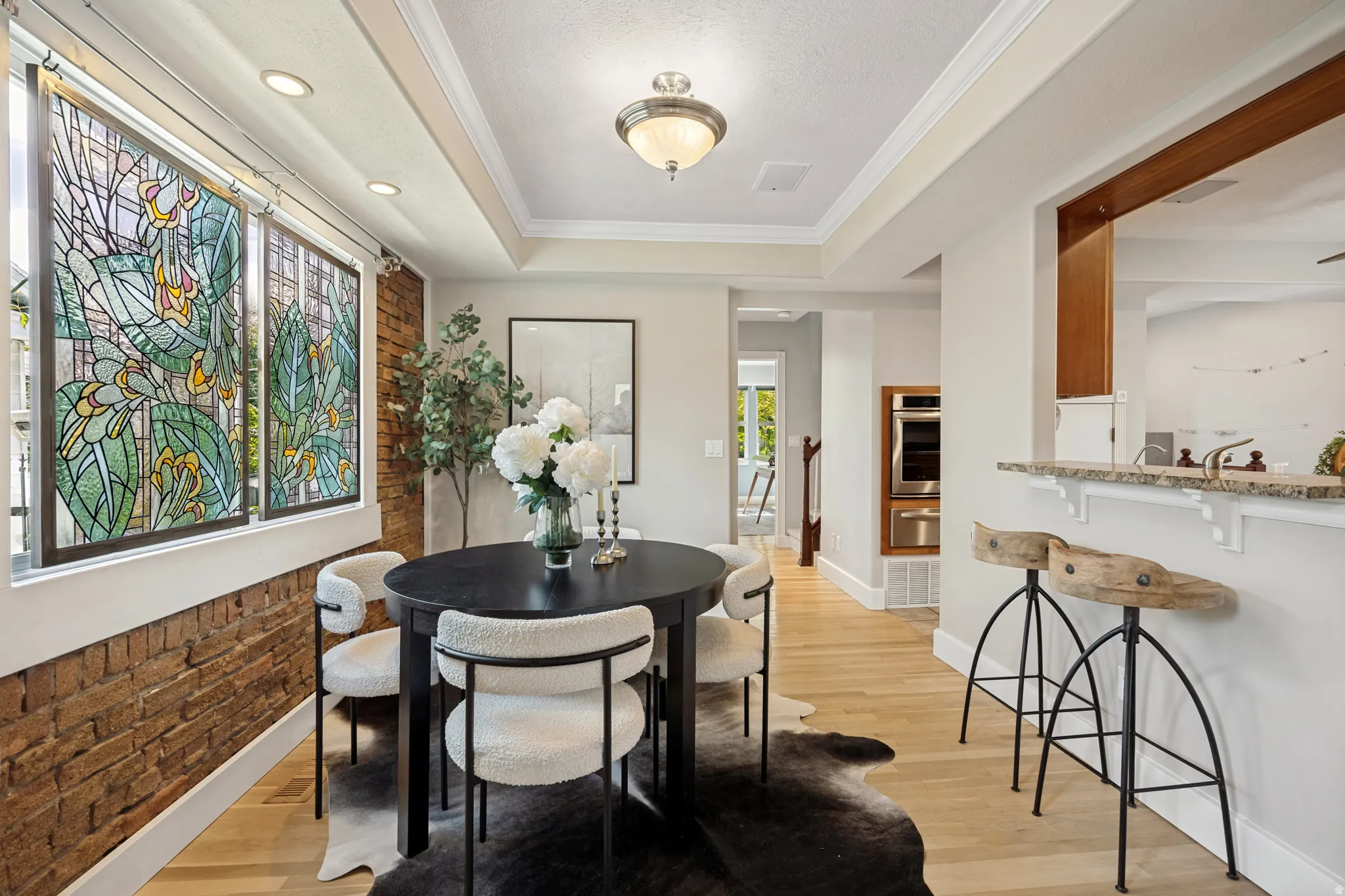 Hardwood-finish flooring, accent brick wall, stained glass window panels, tray ceiling with recessed lighting, and a breakfast bar with stone countertop