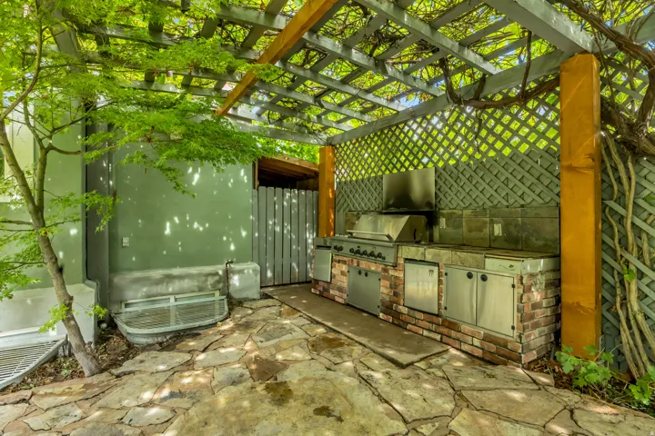 Outdoor kitchen with a built-in grill, brick base, stainless steel cabinetry, and stone countertop