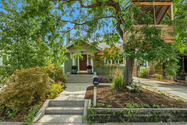 Front exterior with a red entry door, framed by mature trees and established landscaping