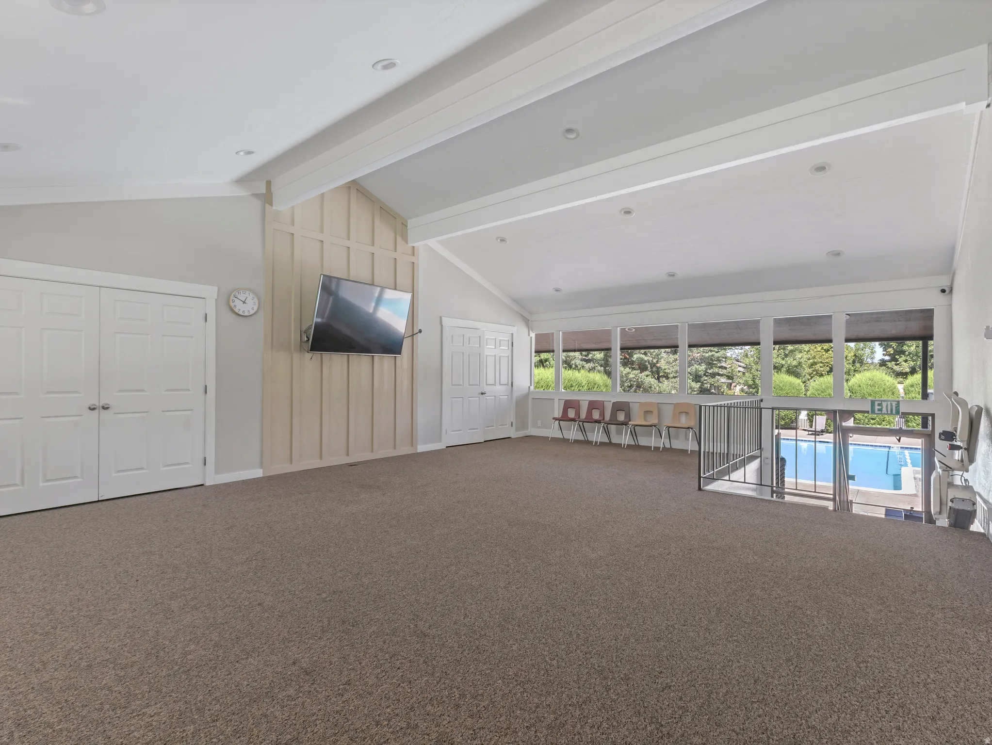 Vaulted ceilings with recessed lighting, large windows, board and batten accent wall, neutral carpeting, and a built-in pool