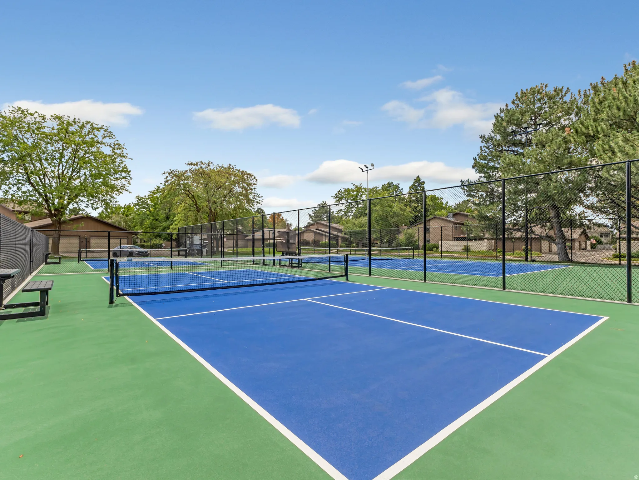 Two vibrant blue and green sport courts with black chain-link fencing, featuring multiple nets and integrated benches