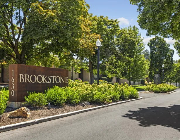 Brookstone community entrance featuring a modern address monument, lush landscaping, mature trees, paved roadways, and decorative street lighting