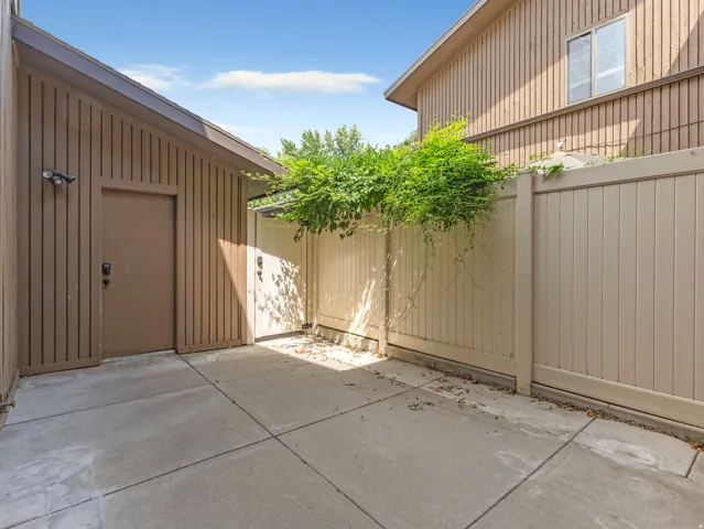 Paved courtyard featuring a privacy fence, wood-paneled exterior, and a security light fixture