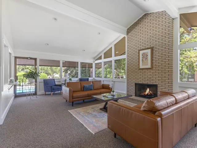 Brick fireplace with a metal insert, vaulted ceilings with exposed beams, and multiple windows with operable shades