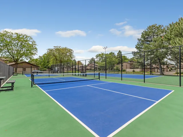 Two vibrant blue and green sport courts with black chain-link fencing, featuring multiple nets and integrated benches