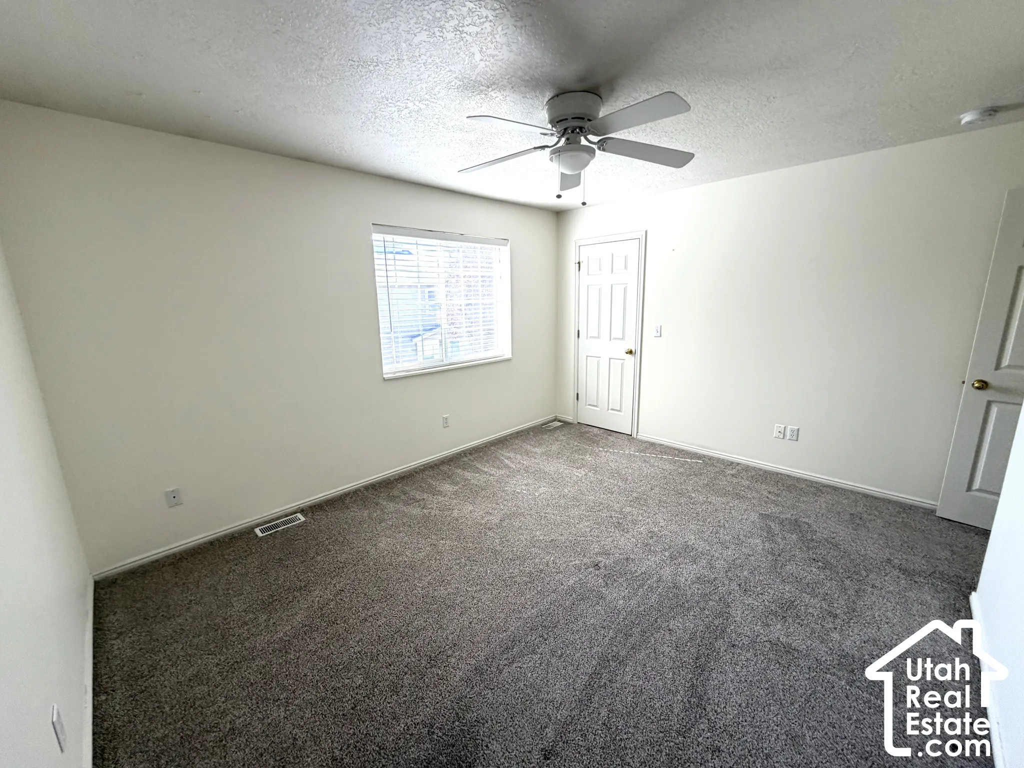 Neutral-toned carpeting, white interior walls, and a ceiling fan with light fixture