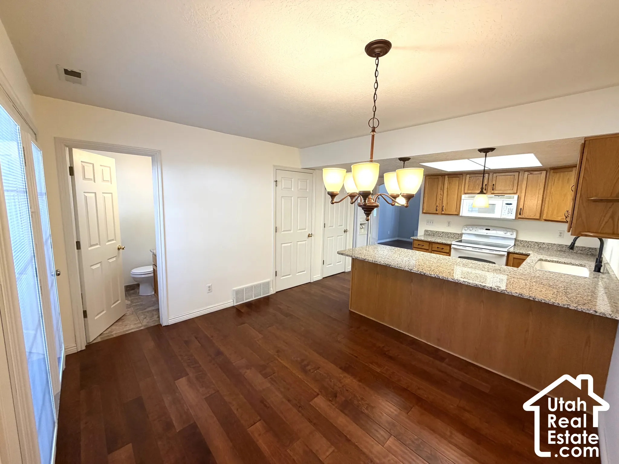 Wood-finish flooring throughout, kitchen with light wood cabinetry, white appliances, and granite-style countertops