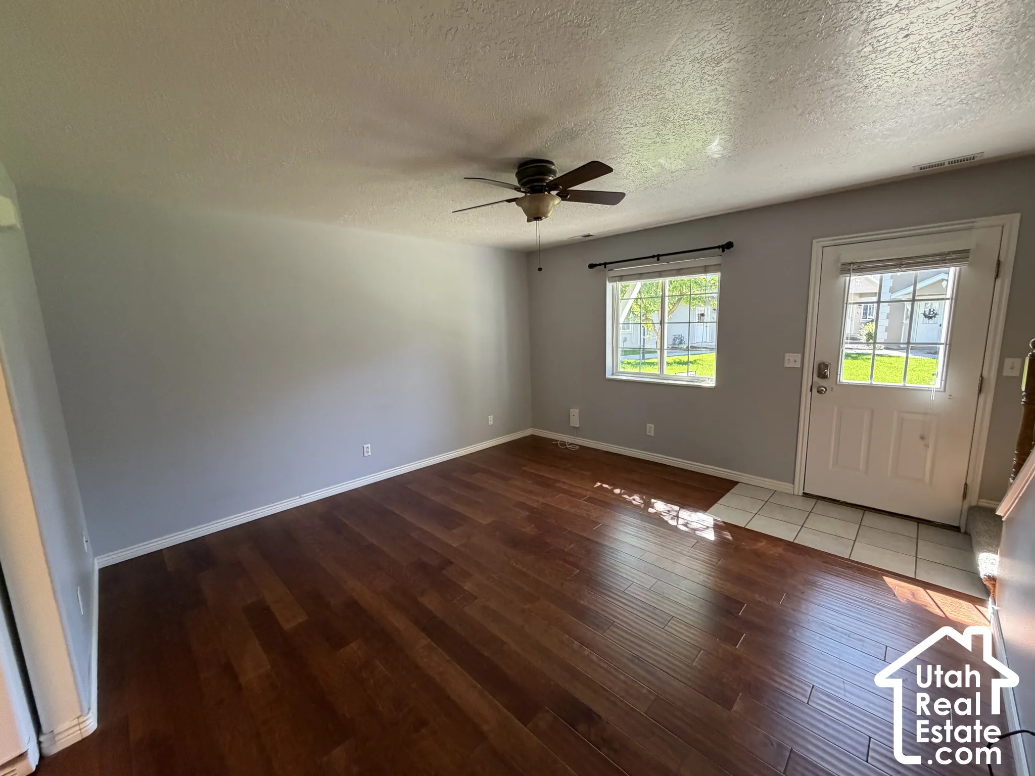 Wood-finish flooring, ceiling fan, white paneled door with window, and a window with blinds