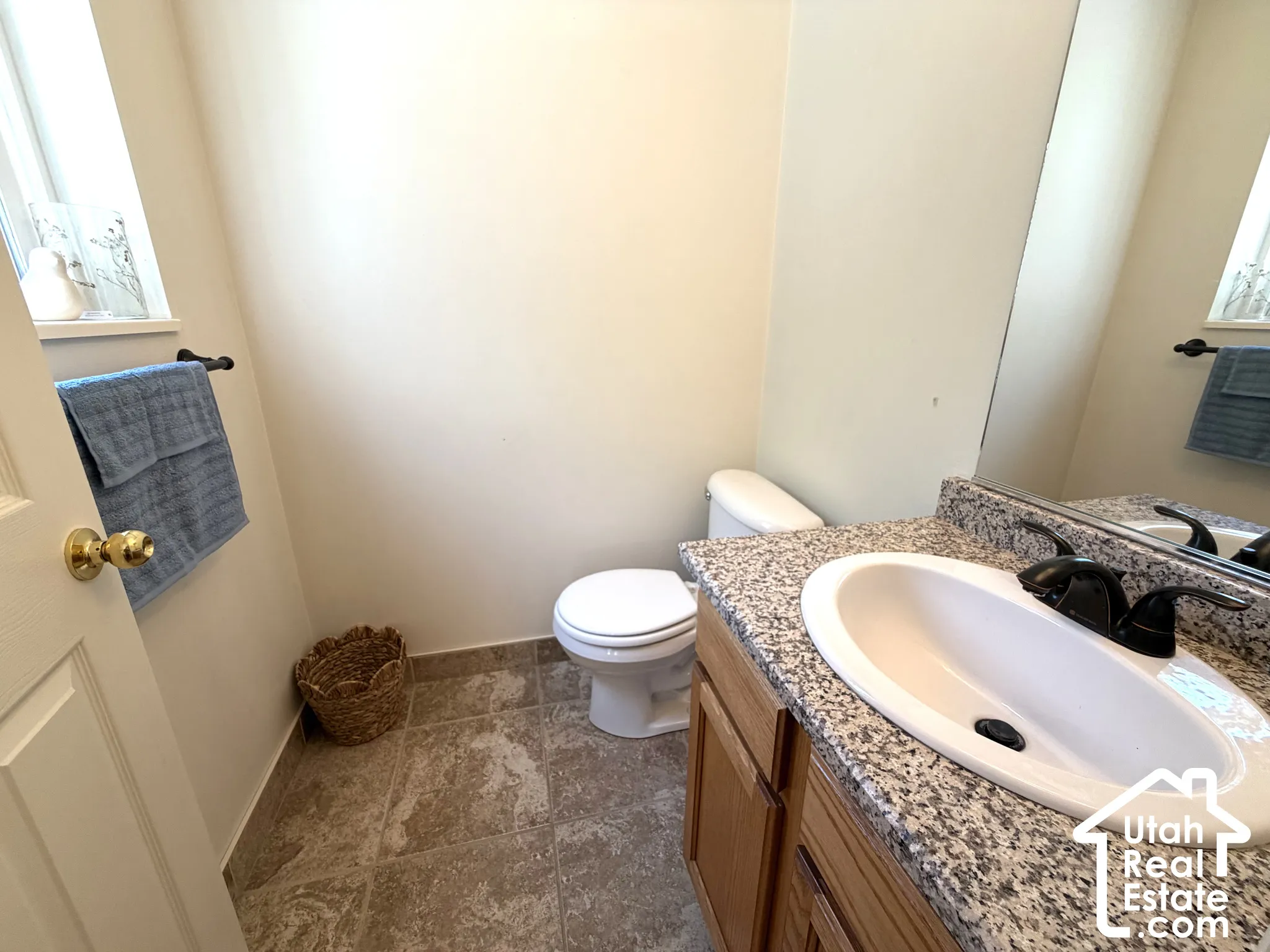Bathroom featuring a vanity with an integrated sink, granite-style countertop, wood-finish cabinetry, ceramic tile flooring, and a window