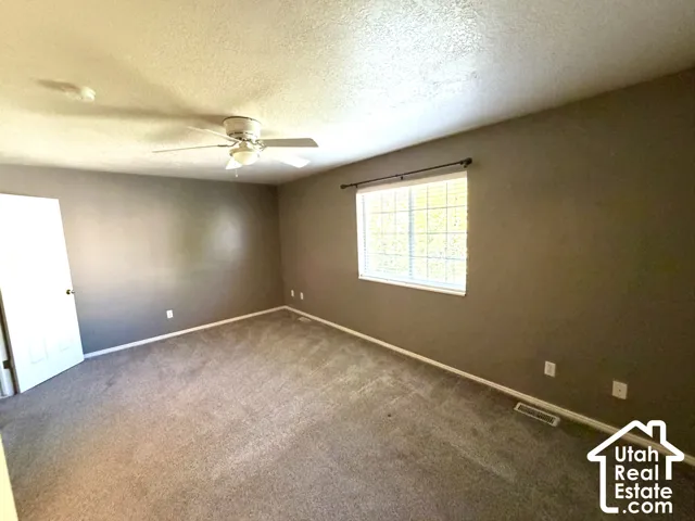 Spacious room featuring neutral carpeting, a ceiling fan with integrated lighting, and a prominent window with blinds
