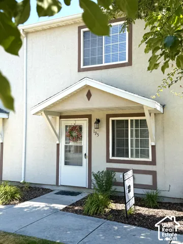 Stucco exterior with brown trim accents, covered entry, and exterior lighting