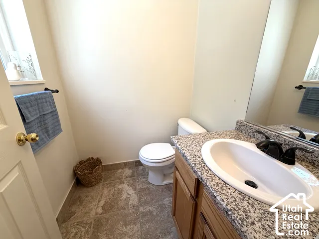 Bathroom featuring a vanity with an integrated sink, granite-style countertop, wood-finish cabinetry, ceramic tile flooring, and a window