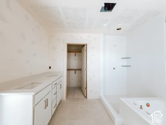 Dual vanity with integrated sinks and white cabinetry, a walk-in shower with subway tile surround, a built-in bathtub, and a separate closet space