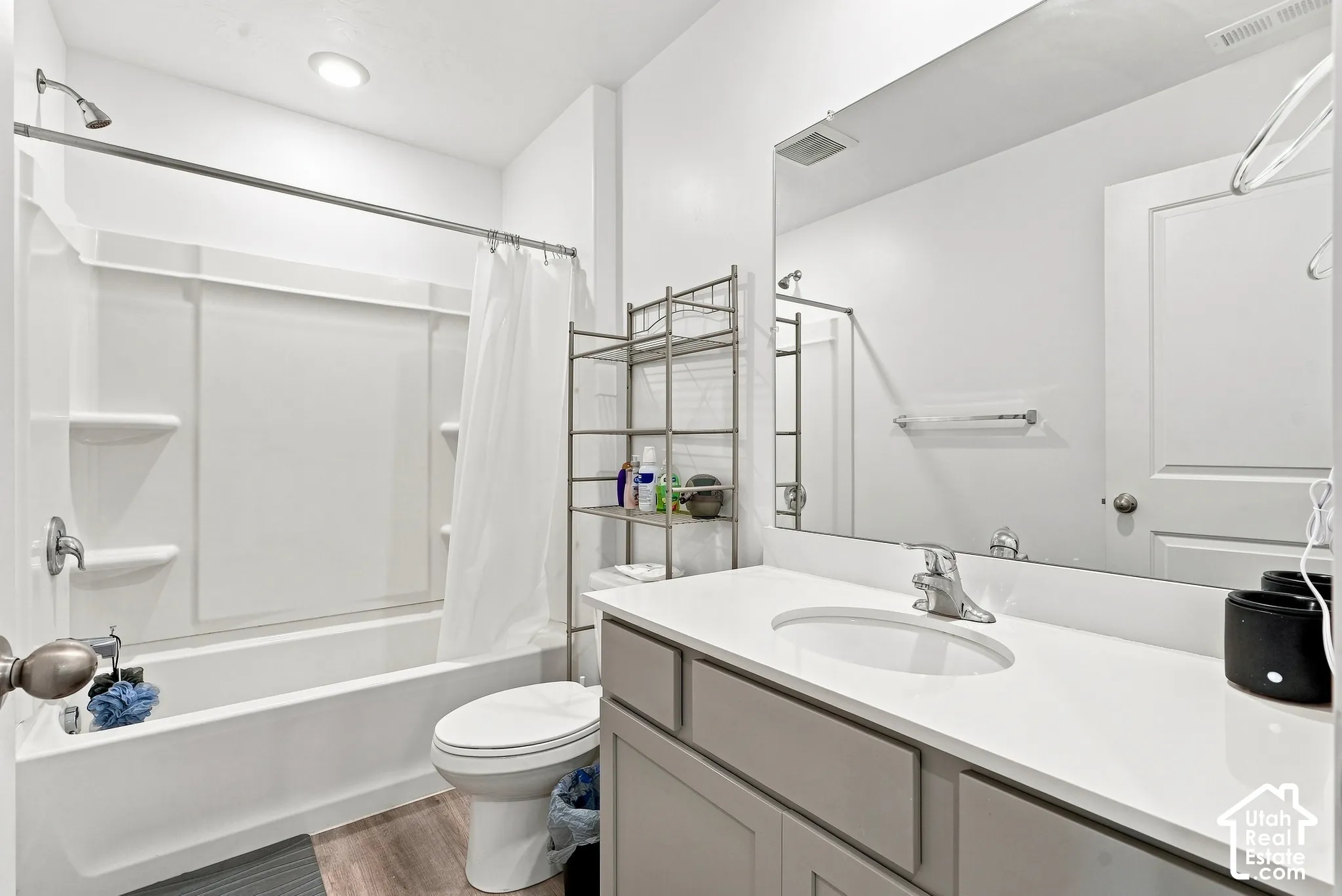 Integrated tub and shower combination, vanity with light gray cabinetry, white countertop, and large wall-mounted mirror