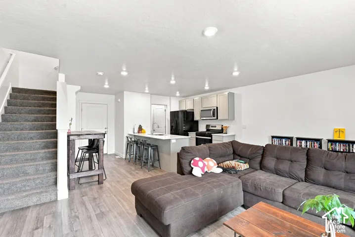 Wood-finish flooring, recessed lighting, white walls, and a gray-carpeted staircase