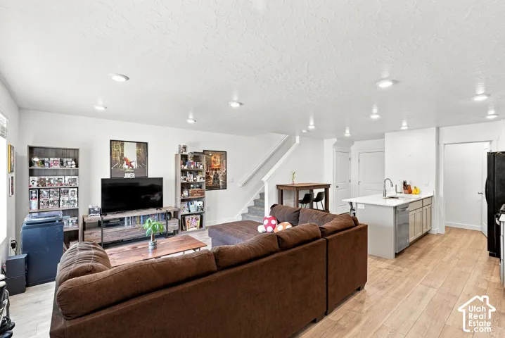 Open concept living space featuring wood-finish flooring, recessed lighting, a modern kitchen island with an integrated sink, and an adjacent staircase
