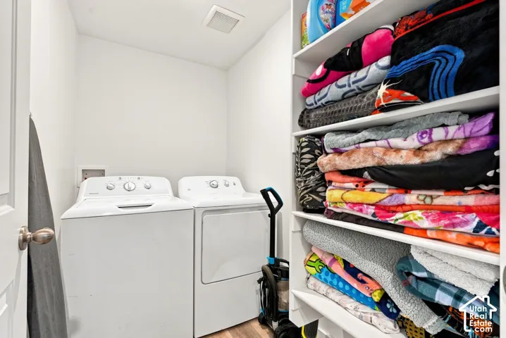 Dedicated laundry area featuring white walls, wood-finish flooring, built-in shelving, and a ceiling-mounted light fixture
