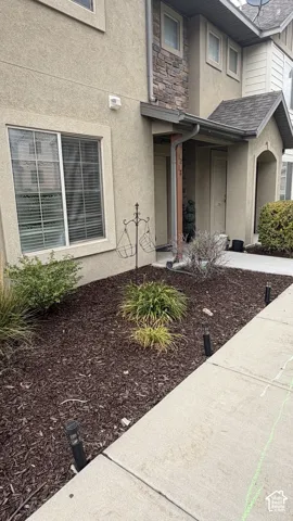 Stucco exterior with stone accents, covered entry, front landscaping with mulch, and sidewalk access