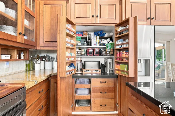 Wood-finish cabinetry with glass-front uppers, light-toned countertop, integrated pantry storage, and stainless steel refrigerator