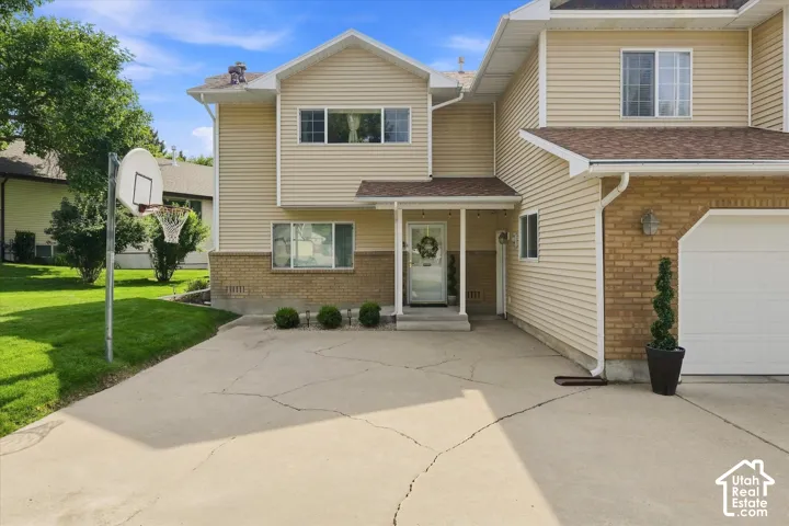 Light-colored siding exterior with brick accents, attached garage with white door, covered front entry, and concrete driveway