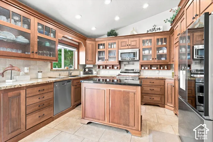 Kitchen featuring wood cabinetry, stainless steel appliances, a center island with a dark countertop, light-toned tile flooring, and recessed lighting