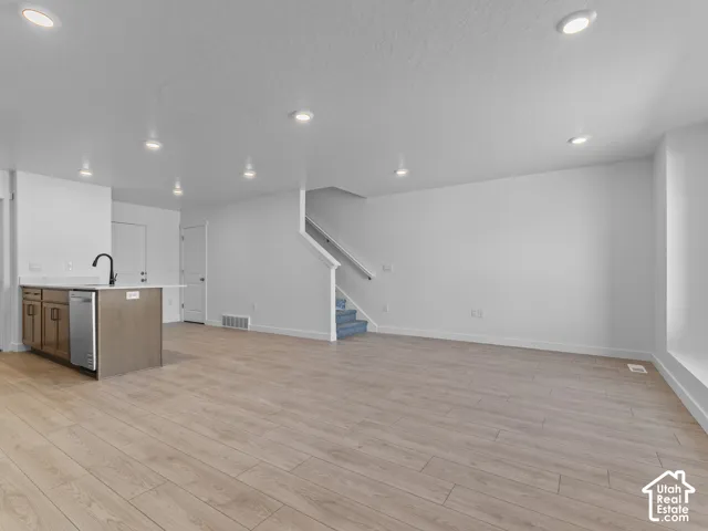 Open-concept living space featuring wood-finish flooring, recessed lighting, a kitchen island with a black gooseneck faucet, and stainless steel appliances