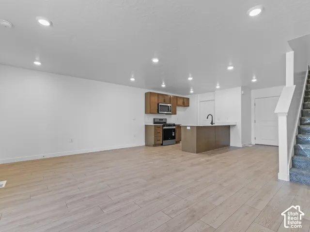 Recessed lighting, wood-finish flooring, kitchen island with sink, stainless steel appliances, and wood cabinetry
