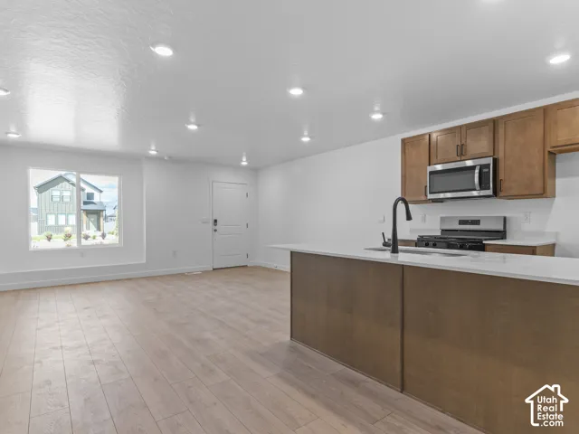 Open-concept living space with wood-finish flooring, recessed lighting, and a kitchen featuring a peninsula with countertop seating, stainless steel appliances, and wood cabinetry
