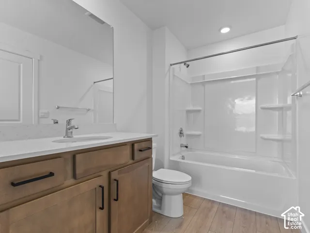 Wood-finish flooring, wood-finish vanity with black hardware, white countertop, integrated sink with chrome faucet, and a combination bathtub/shower