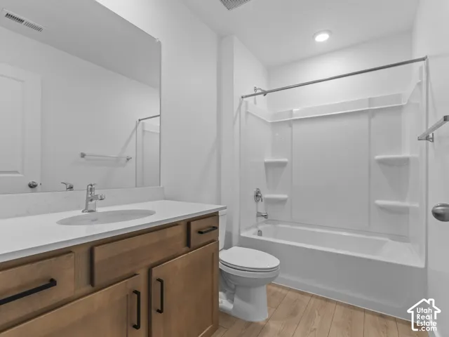 Wood-finish flooring, white vanity countertop, wood-finish cabinetry with matte black hardware, integrated vanity sink, and a white bathtub with shower surround