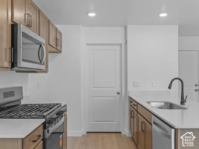 Kitchen featuring wood-finish cabinetry, stainless steel appliances, light-toned countertops, and a stainless steel sink with a matte black faucet
