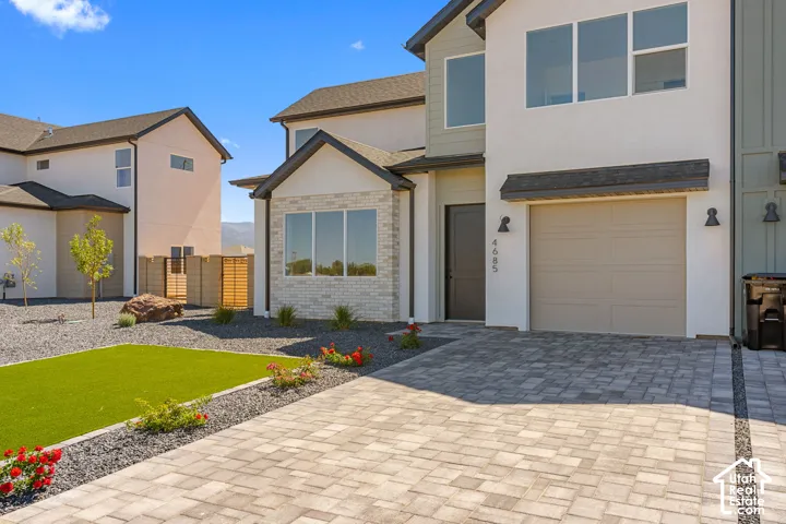 Modern exterior with stucco and brick facade, paver driveway, artificial turf landscaping, and prominent windows