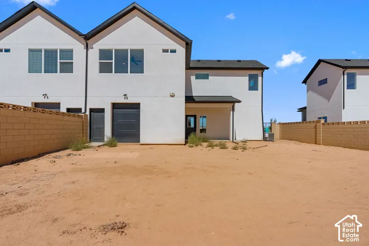 Expansive undeveloped land with a perimeter block fence, adjacent to a contemporary two-story residence with a dark garage door