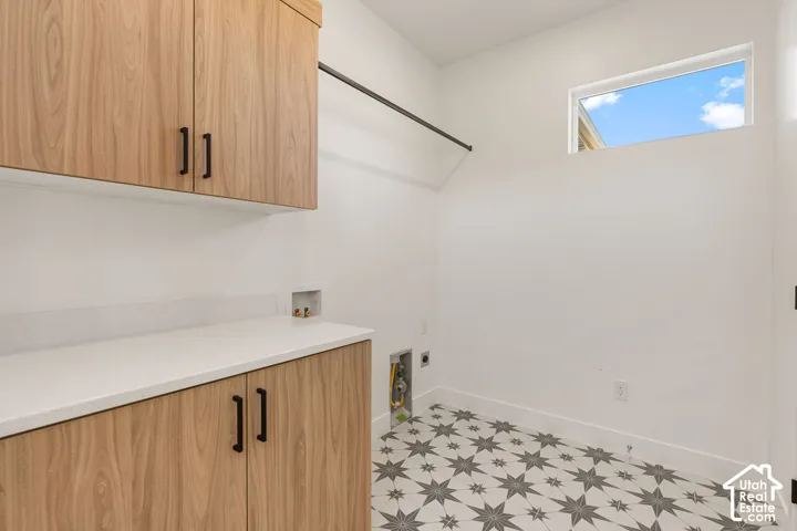 Wood-finish cabinetry with matte black hardware, white countertop, patterned floor tile, and a high window