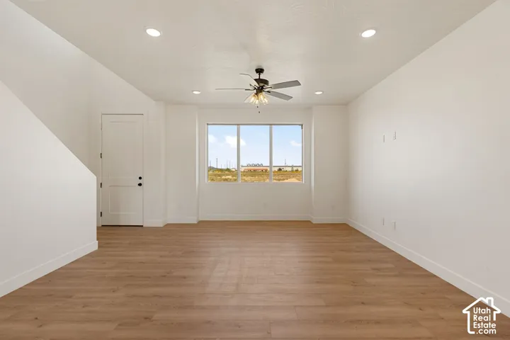 Recessed lighting, wood-finish flooring, a ceiling fan with integrated lighting, a large window, and a two-panel door with black hardware