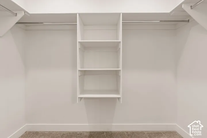 Built-in white shelving system with multiple tiers, integrated hanging rods, and a neutral carpeted floor