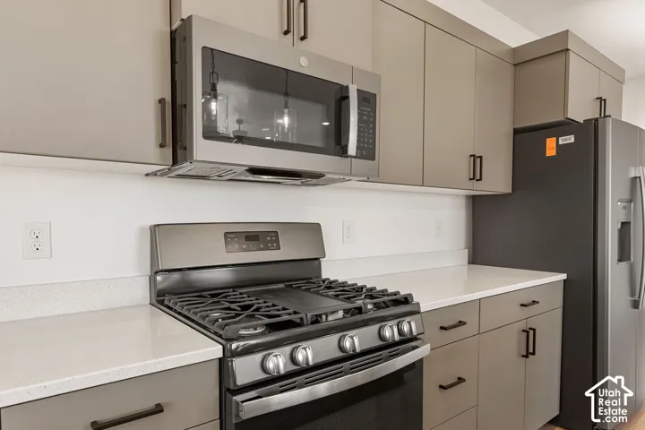 Kitchen featuring light gray cabinetry, white countertops, a stainless steel range, a stainless steel microwave, and a black refrigerator