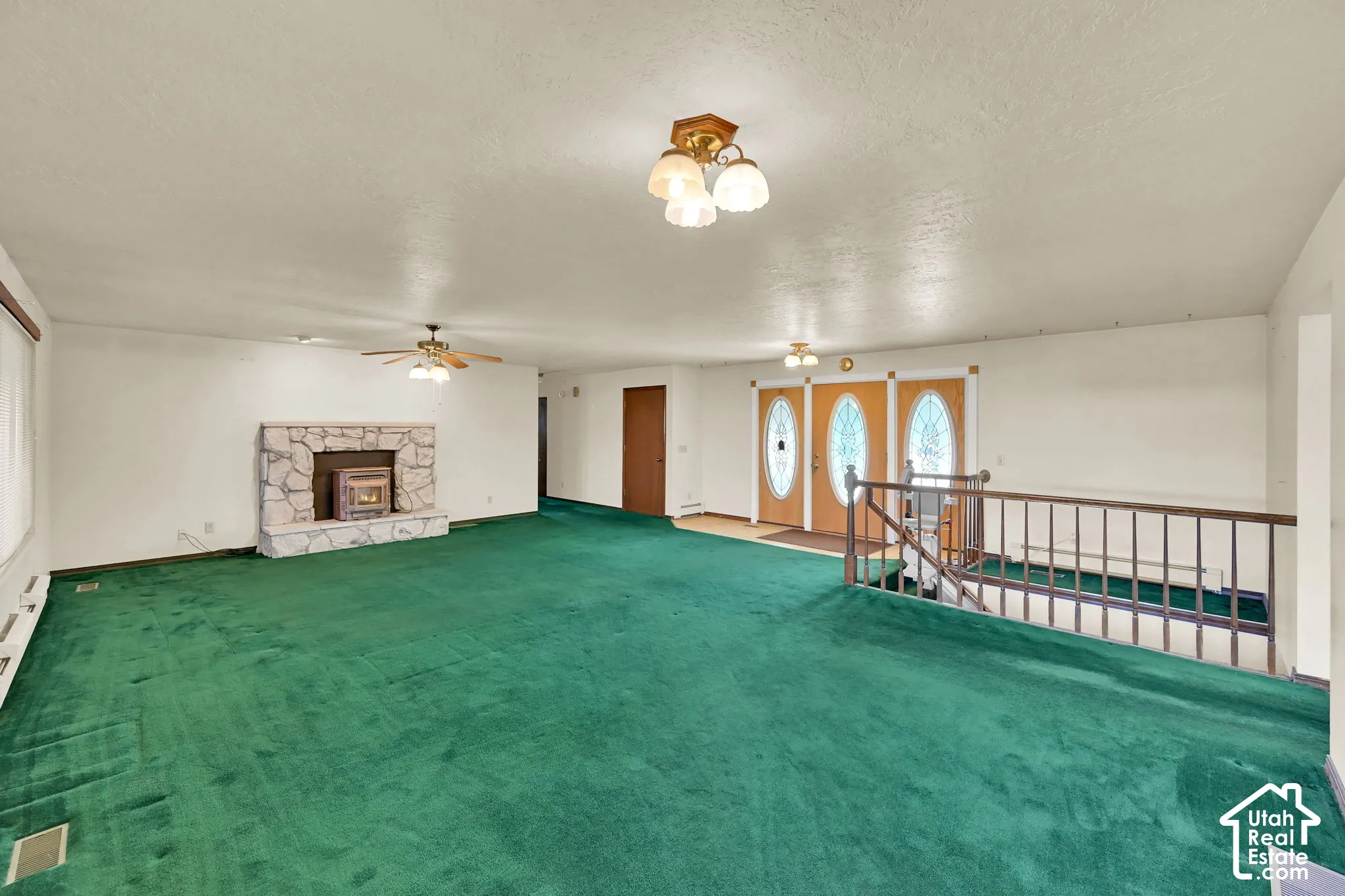 Spacious room with a stone fireplace, wood-burning insert, ceiling fan, and a wood banister