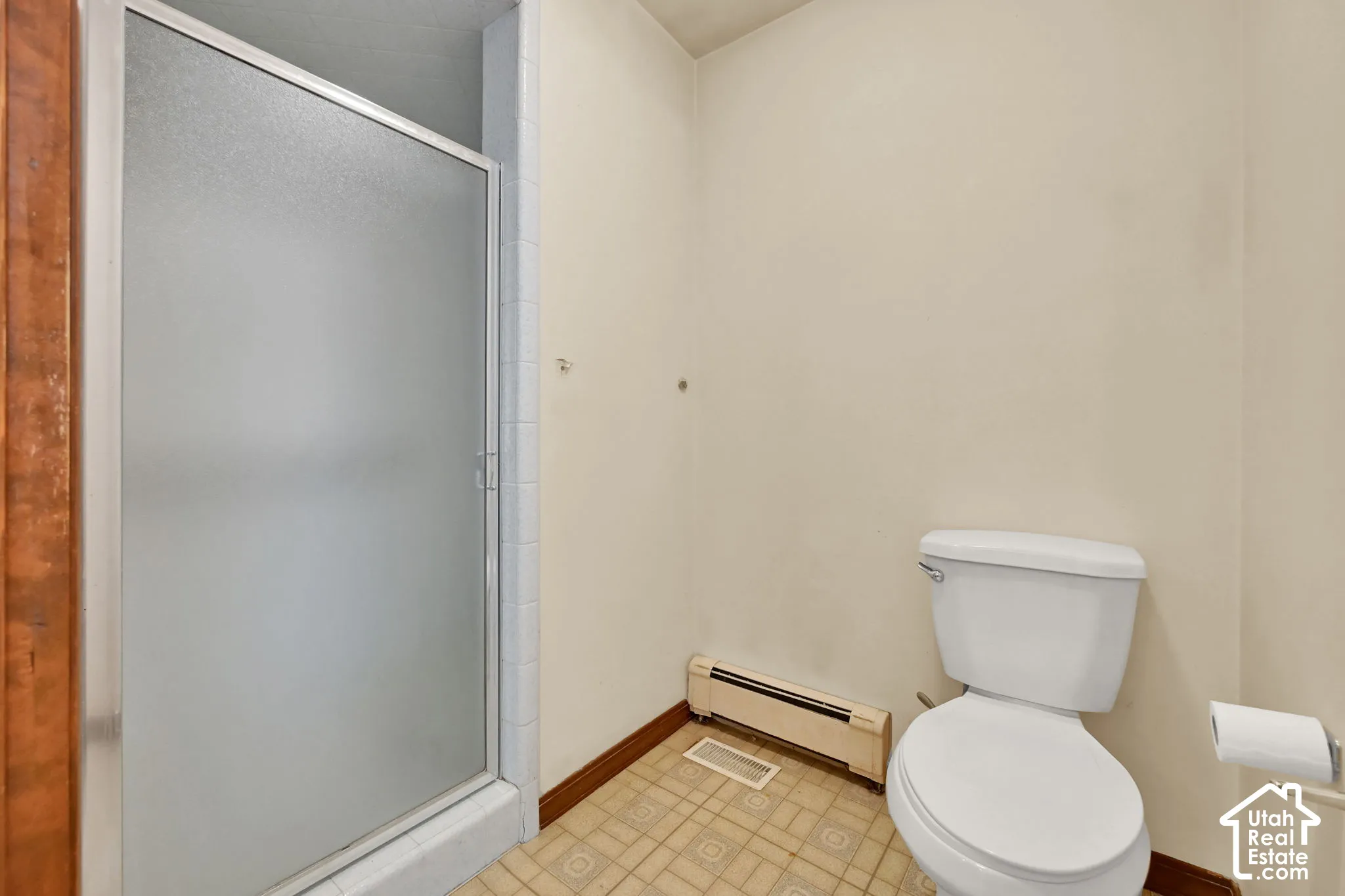 Shower enclosure with a frosted glass door, white toilet, and patterned tile flooring