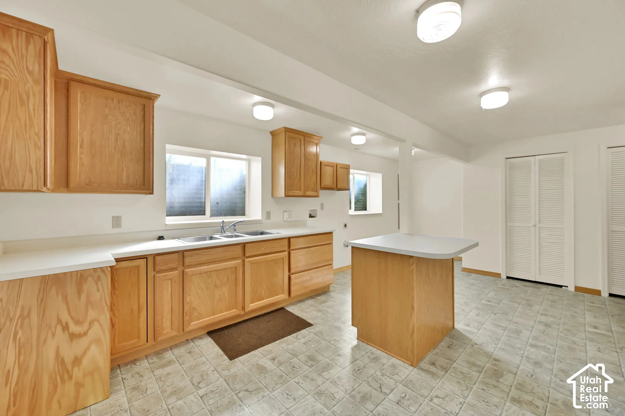 Kitchen featuring wood cabinetry, white countertops, dual basin sink, central island, and tiled flooring