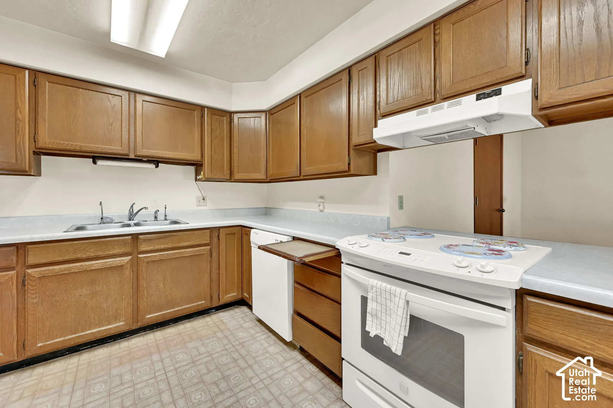 Kitchen featuring wood-finish cabinetry, solid surface countertops, a stainless steel sink, and white appliances