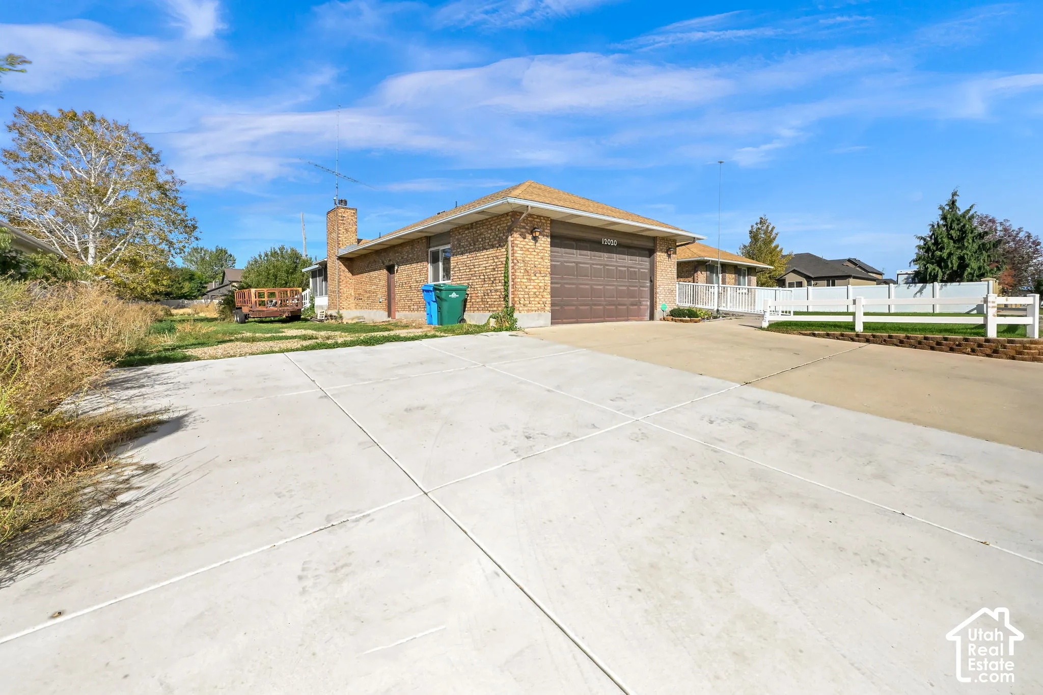 Brick exterior with an attached garage, concrete driveway, and white fencing