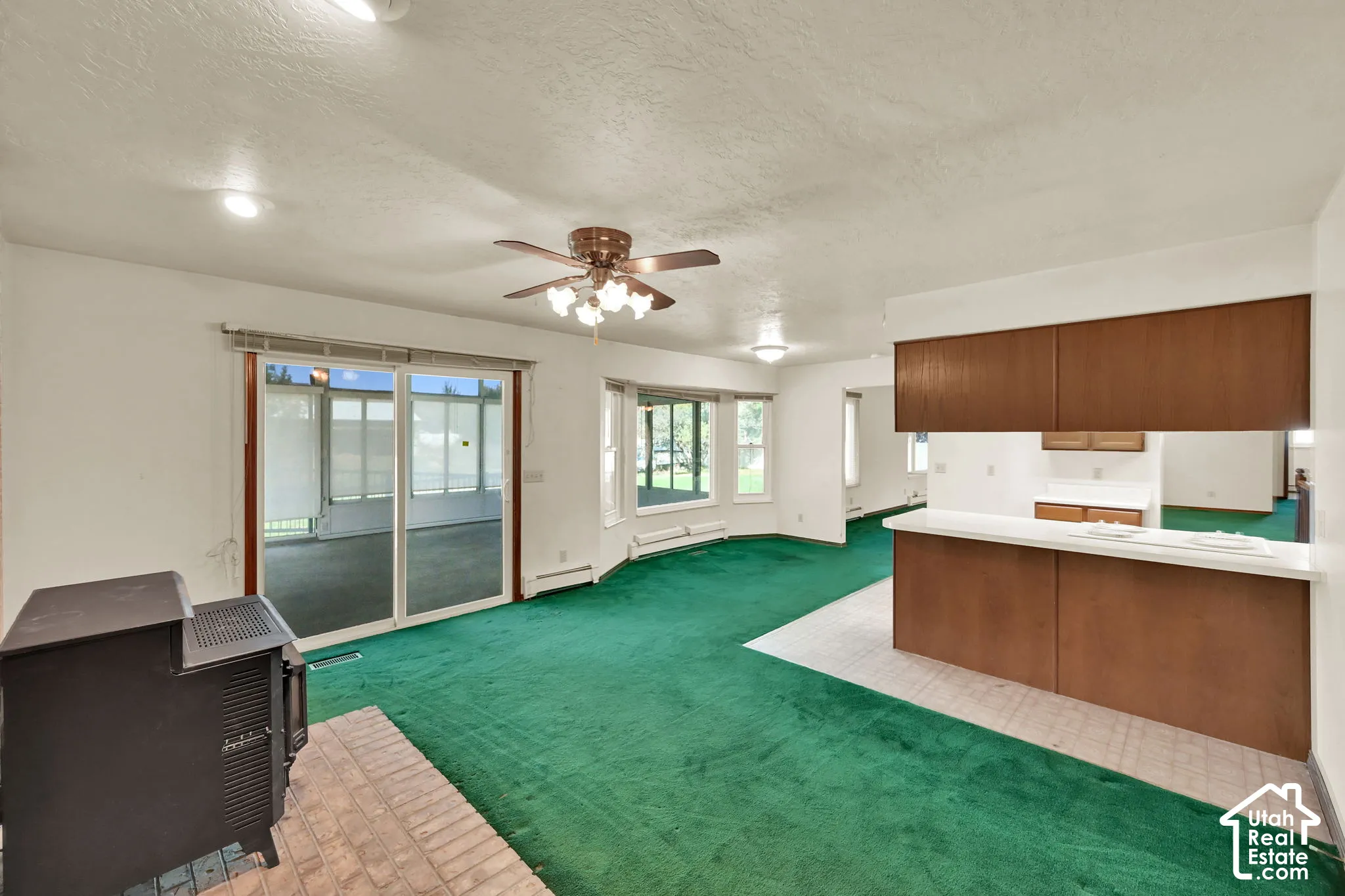 Open-concept living area with a wood-burning stove on a brick hearth, sliding glass doors, and a ceiling fan