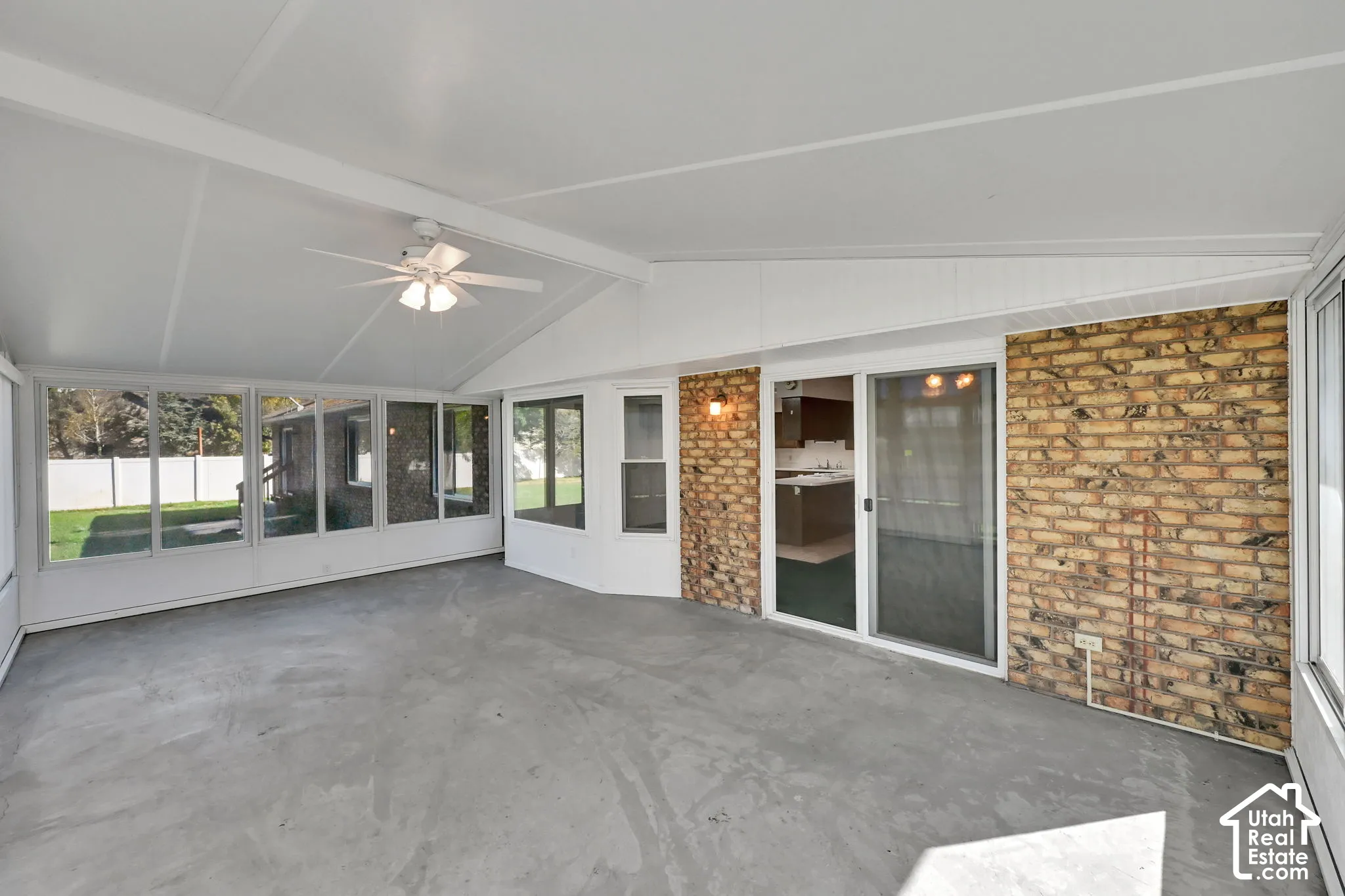 Spacious sunroom featuring a vaulted ceiling with a ceiling fan, concrete flooring, and multiple window panels