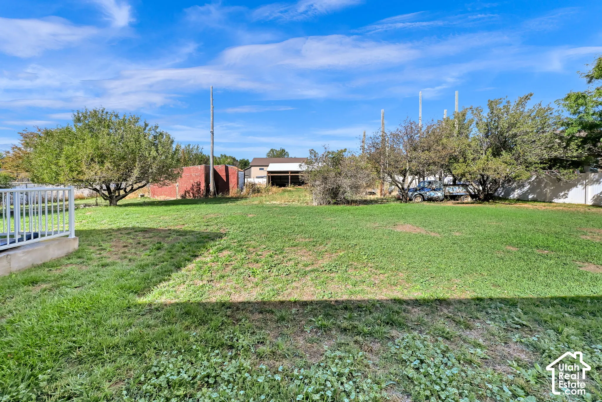 Expansive green space featuring mature trees and a partial white fence