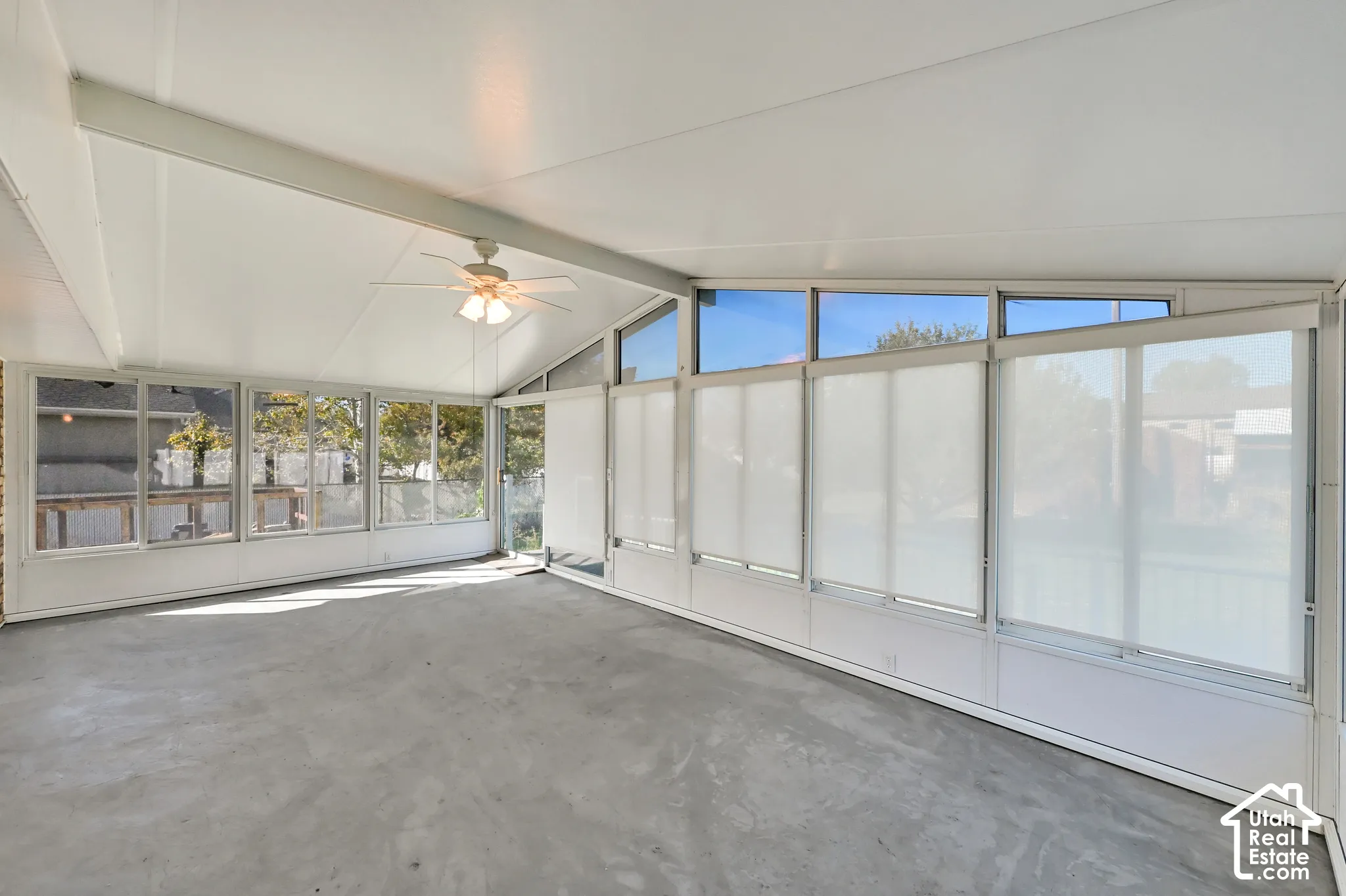 Enclosed sunroom featuring a vaulted ceiling with a fan, concrete flooring, and multiple windows with adjustable privacy screens