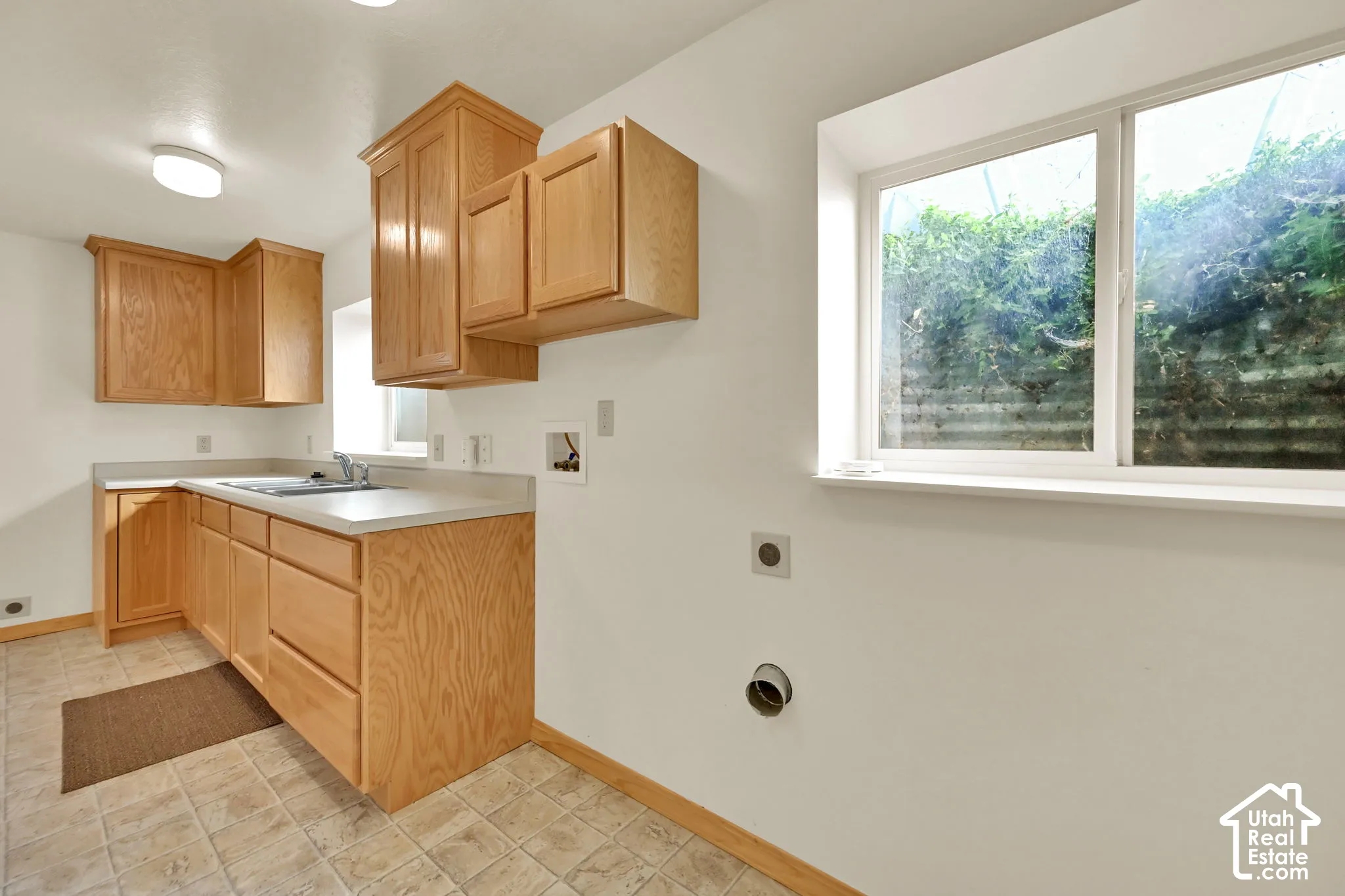 Utility room with light wood-finish cabinetry, a utility sink, and a light-toned countertop