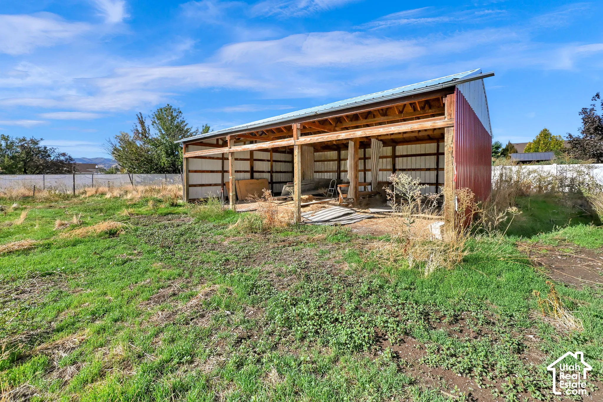 Open-air barn structure featuring a metal roof and red corrugated siding
