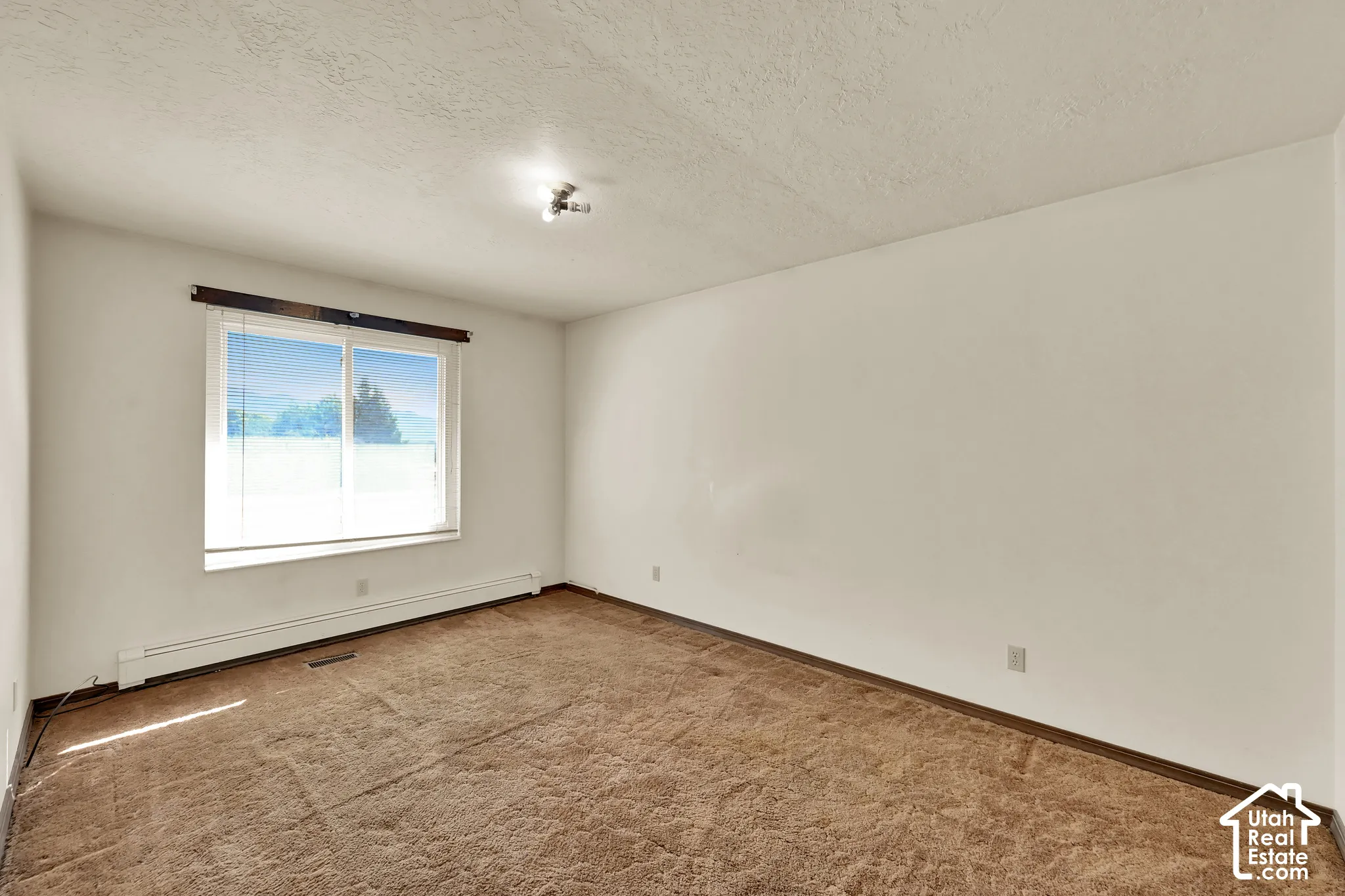 Spacious room featuring carpeted flooring, a large window with blinds, and white painted walls
