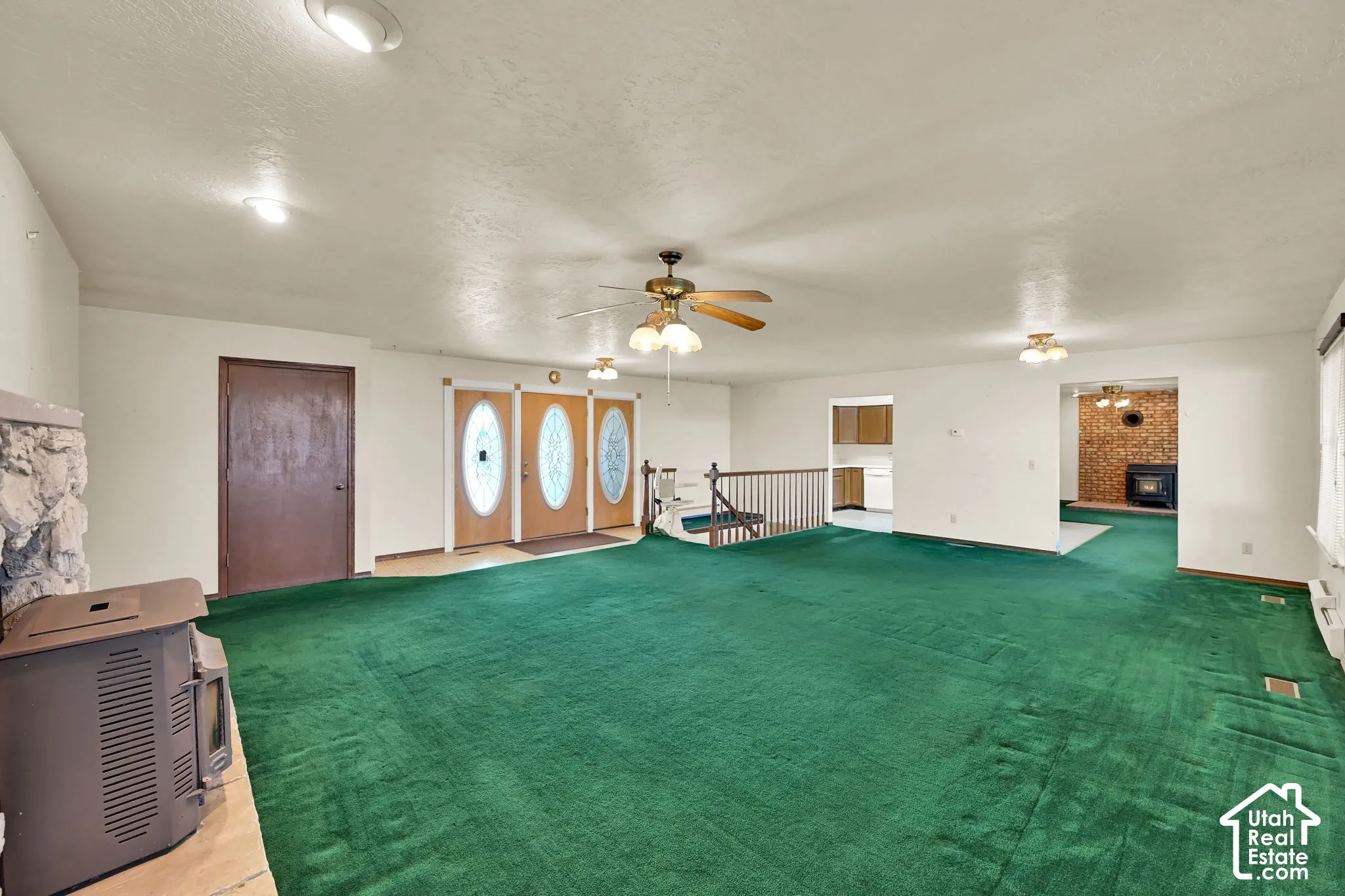 Expansive carpeted living area with overhead lighting, a stone fireplace, and wood entry doors featuring decorative glass